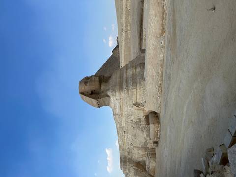       The Great Sphinx of Giza with a pyramid in the background under a clear blue sky.
  