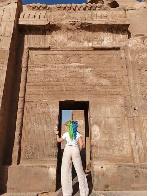 Person observing a large stone wall with Egyptian hieroglyphs.