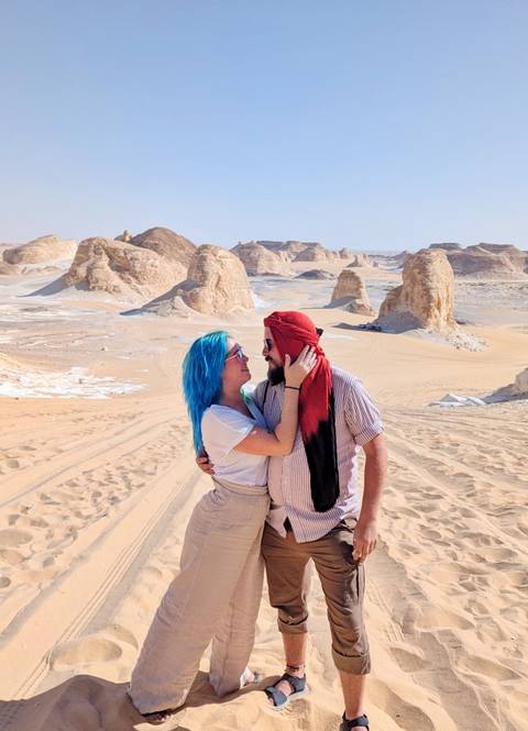 Couple standing in a desert landscape with rock formations.