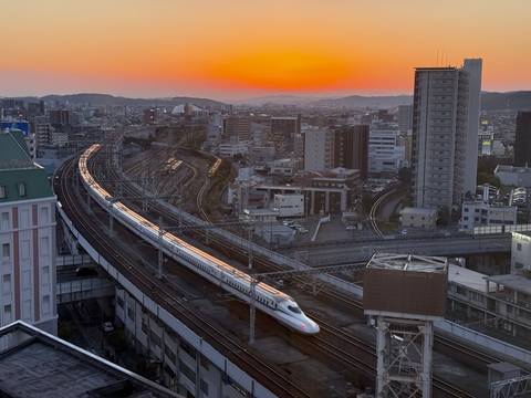 Bullet train moving through a city at sunset.