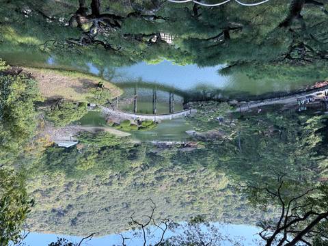 Scenic landscape of a Japanese garden with a bridge over a pond, surrounded by greenery.