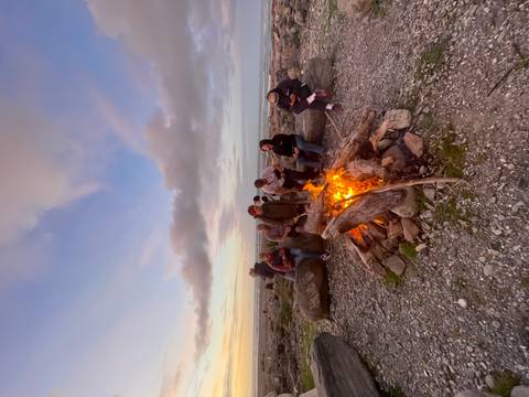 People sitting around a campfire on a beach at sunset.