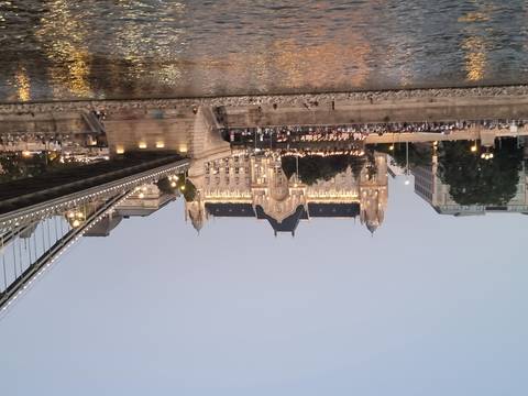 City view of a historic building along a river, with a bridge.