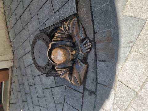 Bronze sculpture of a man peeking out of a manhole.