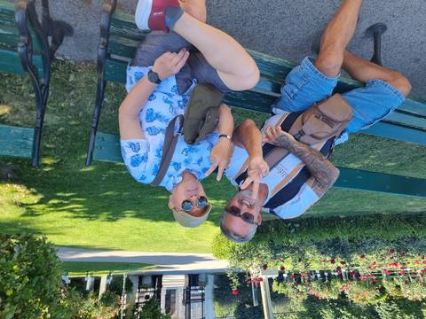 Two men casually posing and smiling on a park bench.