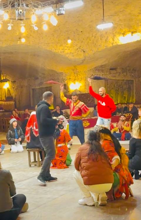       People dancing in traditional attire indoors.
  