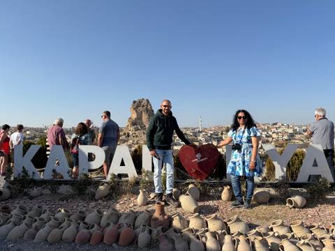       People posing with Cappadocia sign and rock formations.
  