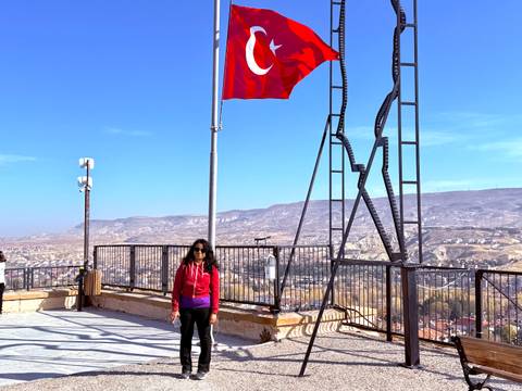       A person posing next to Turkish flag and scenic view.
  