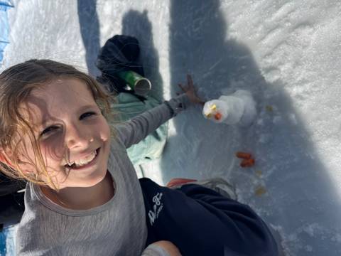 Girl making a small snow figure with visible carrots and fruits.