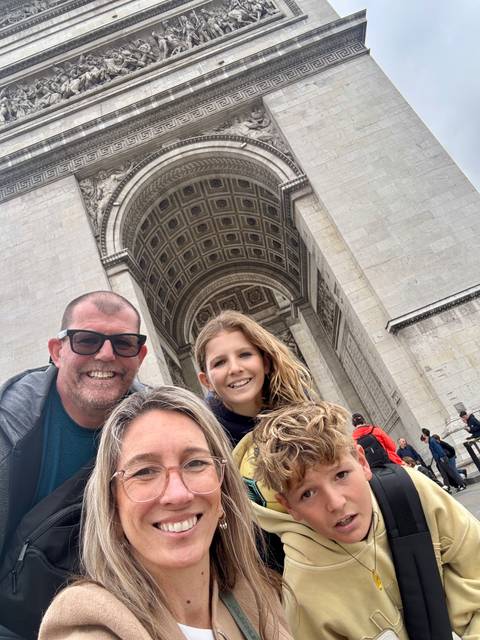 A family taking a selfie with the Arc de Triomphe in the background.