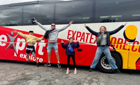 Family jumping in front of an 'Expat Explore' bus.