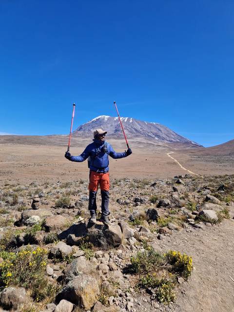 Person standing with arms raised, Mount Kilimanjaro in the background.