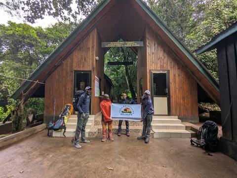 Group of people holding a sign in front of a wooden building.
