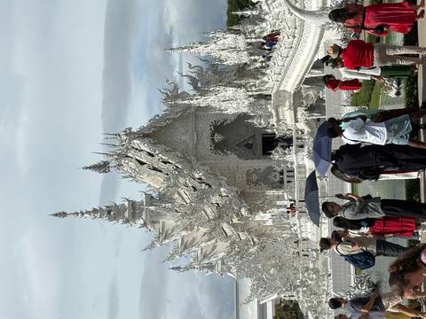 Intricate white temple with people standing and walking around.