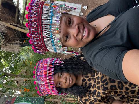 Two people wearing traditional colorful headdresses with a natural background.