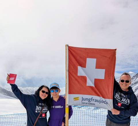 Family posing with a Swiss flag on a snowy mountain backdrop.
