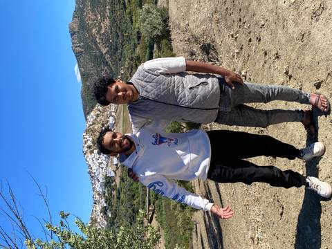 Two men posing with a village in the background.