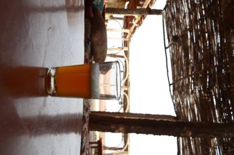A glass half filled with beer on a rustic table, with a wooden structure in the background.