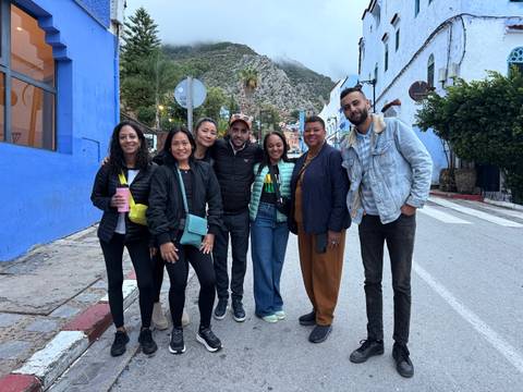       Group of people posing in front of blue buildings in a street.
  
