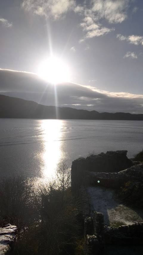 Lake with sunlight reflection surrounded by hills.