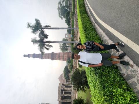 Couple posing with a historic tower and gardens.