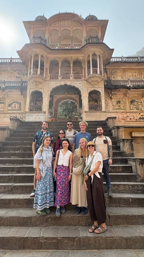 Group of people sitting on stairs in front of an ornate Indian building