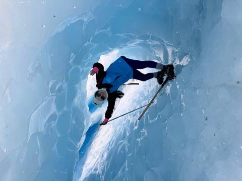 Person exploring a blue ice cave with ice axe