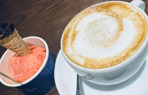A cappuccino and strawberry ice cream on a table.
