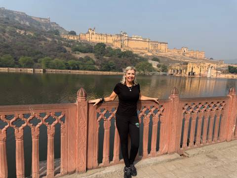 Person posing in front of Amer Fort by a lake.
