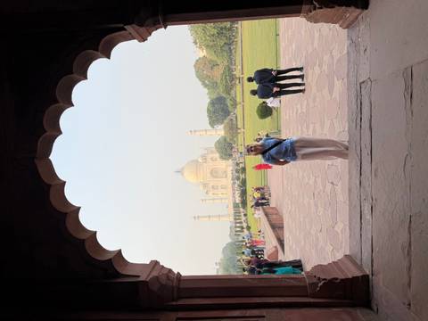 Person standing in an arch with a distant view of the Taj Mahal.
