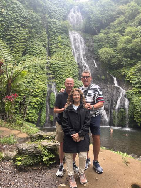 Three people in front of a green waterfall landscape.