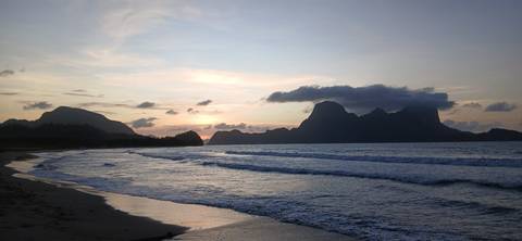 Beach at sunset with waves and distant cloudy mountains.