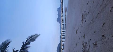 Beach at dusk with a pier extending into the water, mountains in the distance.