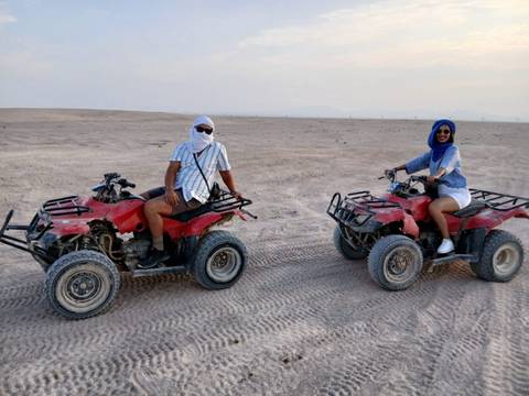      Two people riding quad bikes in a desert landscape.
  