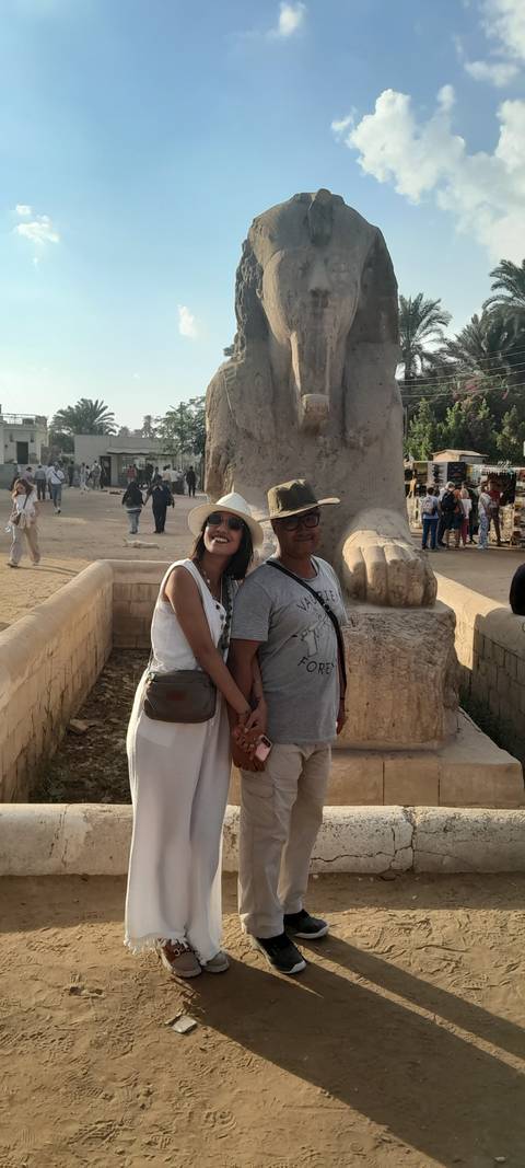       Couple posing in front of a large ancient statue with tourists around.
  