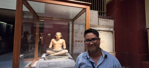 Man standing next to an ancient Egyptian statue in a museum.