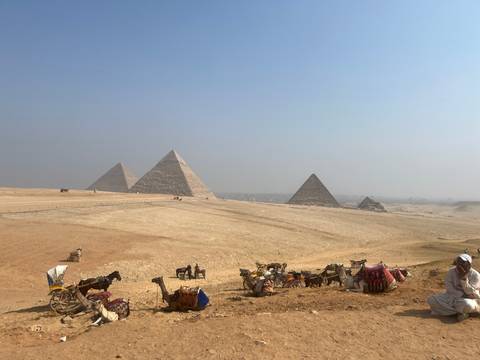 Giza Pyramids viewed from a desert with camels and tourists.