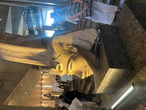       Partially damaged ancient statue inside a well-lit museum.
  