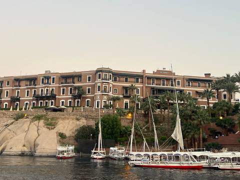       A grand hotel building by the water with boats docked nearby.
  