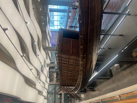       Ancient wooden boat displayed in a modern museum.
  