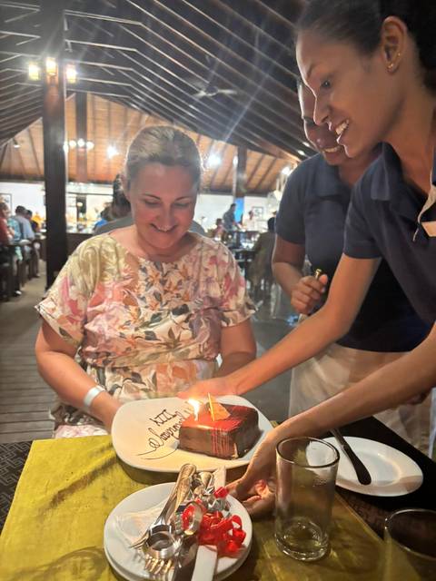 Woman smiling while receiving a small cake with a lit candle.