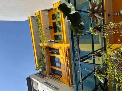 Yellow building with balconies and plants against a blue sky.