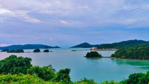       Serene lake view with forest and distant hills under a cloudy sky.
  