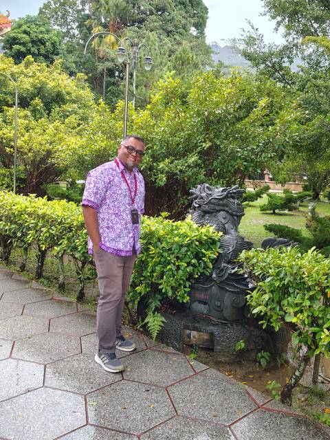       Man posing near bushes and a garden statue.
  