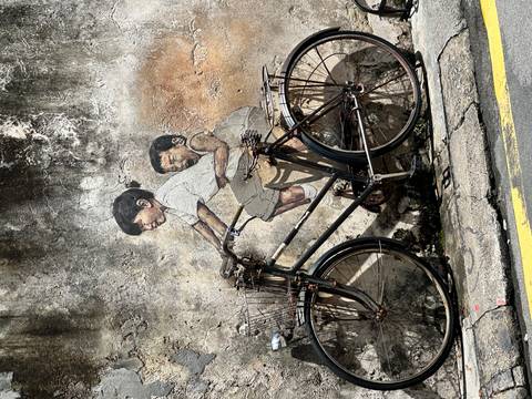       Street mural of children on a bicycle on a textured wall.
  