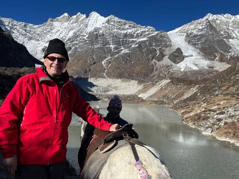       Two people on horseback near a lake in snowy mountains.
  