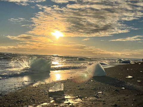 Icebergs on black sand beach during sunset.