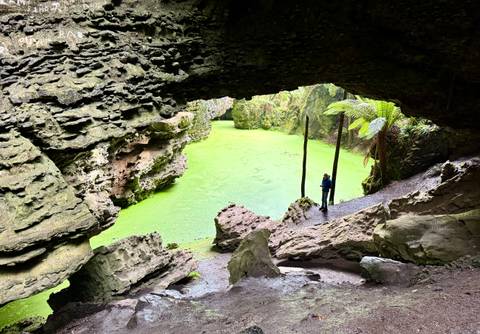       Person standing at the edge of a vibrant green lagoon inside a cave.
  