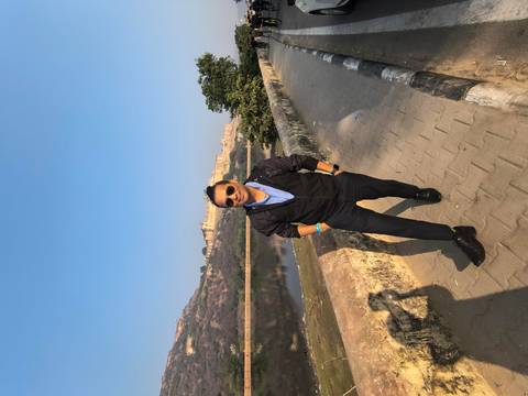 Person posing by a riverbank with a fort in the background.