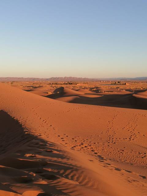 Dunes and distant mountains in a desert under a clear sky.